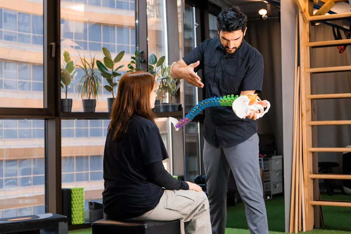 A chiropractor holding and explaining a model of the spine to a patient
